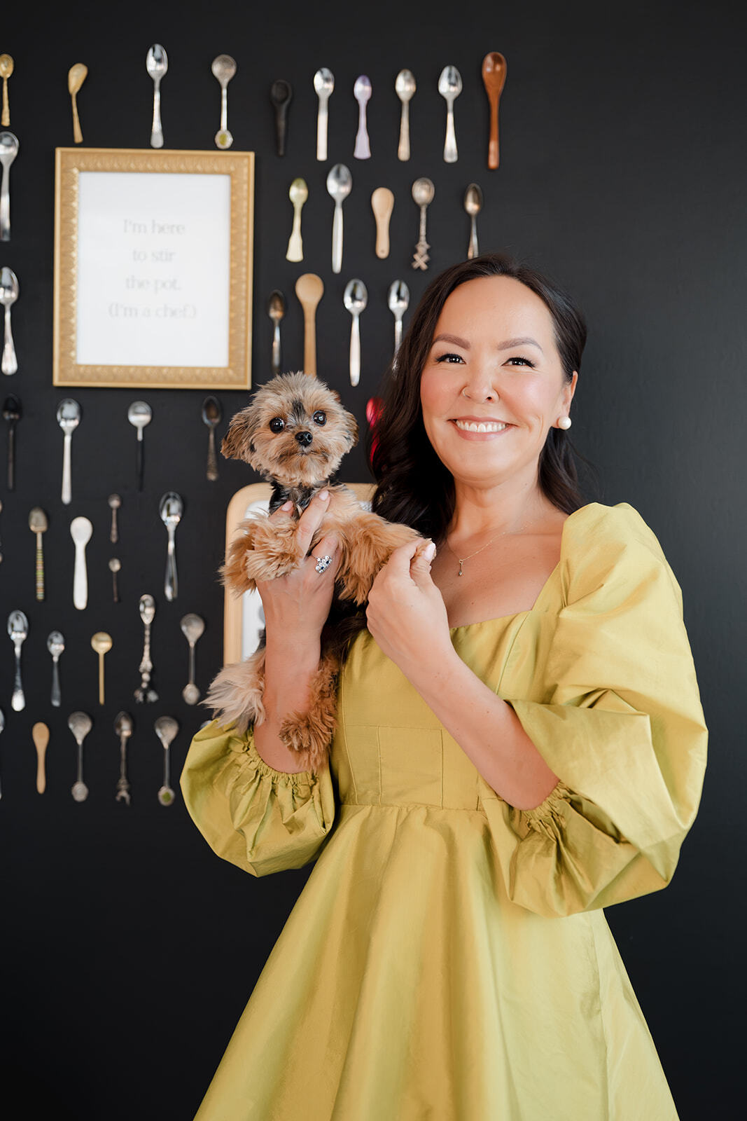 Founder Janice holding her small dog in front of a wall of tiny spoons