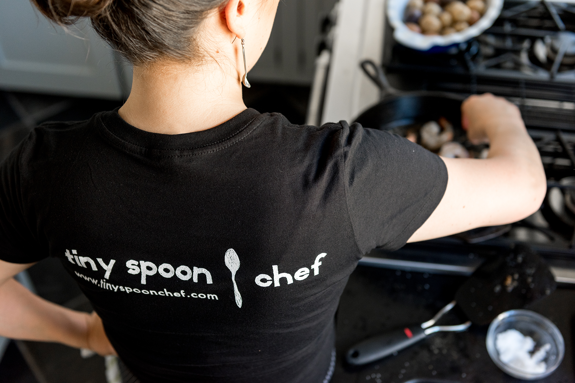 Tiny Spoon chef cooking at a gas stove, seen from behind
