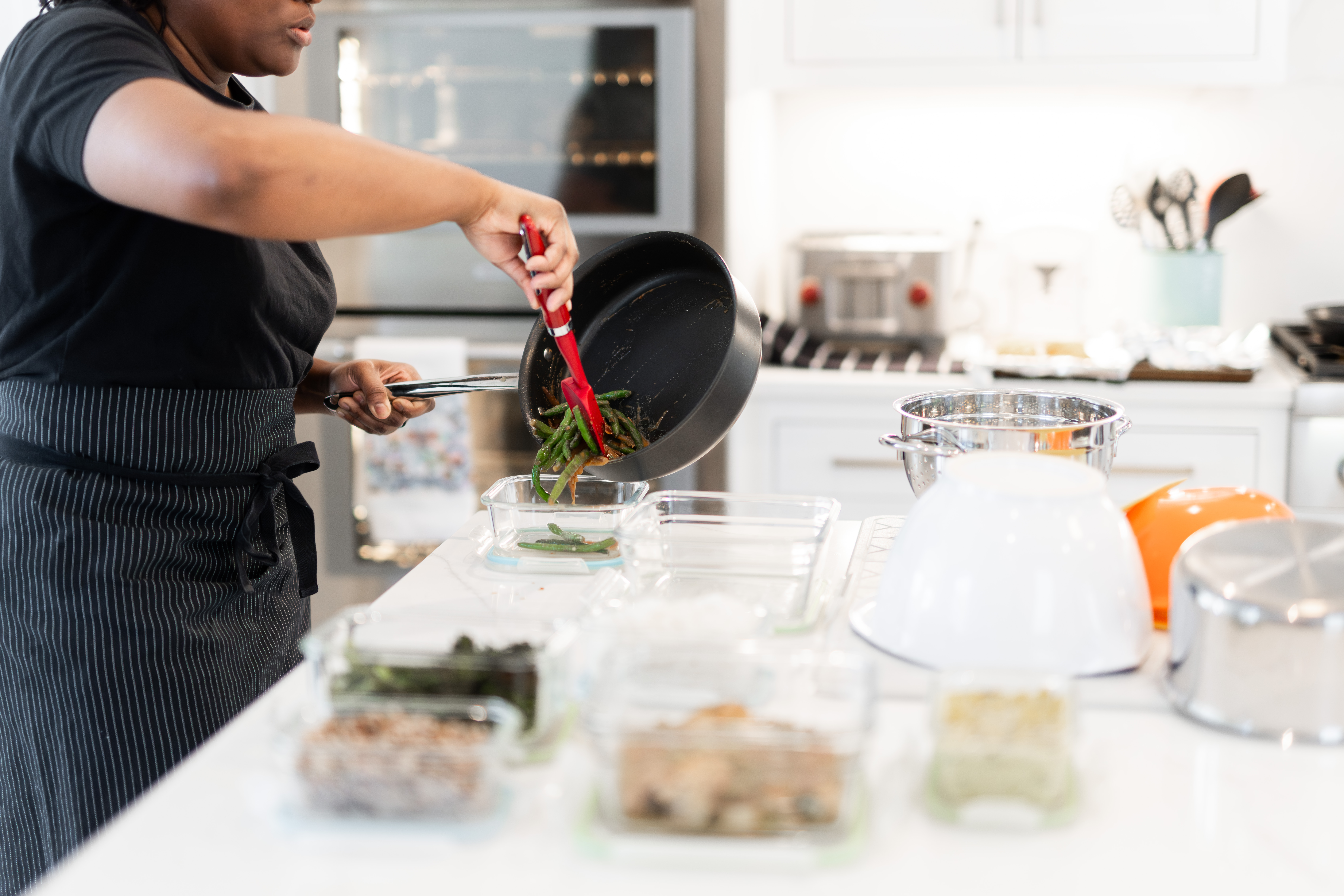 Chef stirring a pan on the stove in a bright white kitchen
