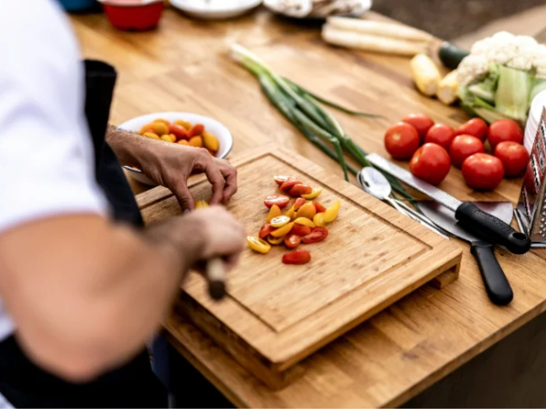 Chef slicing cherry tomatoes and green onions on a wooden cutting board